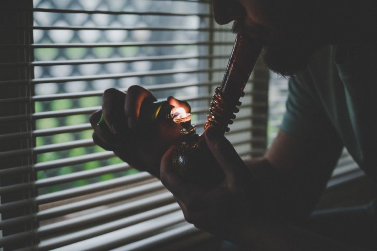 cannabis and anxiety - a person takes a hit of a pipe near a window in a dark room.