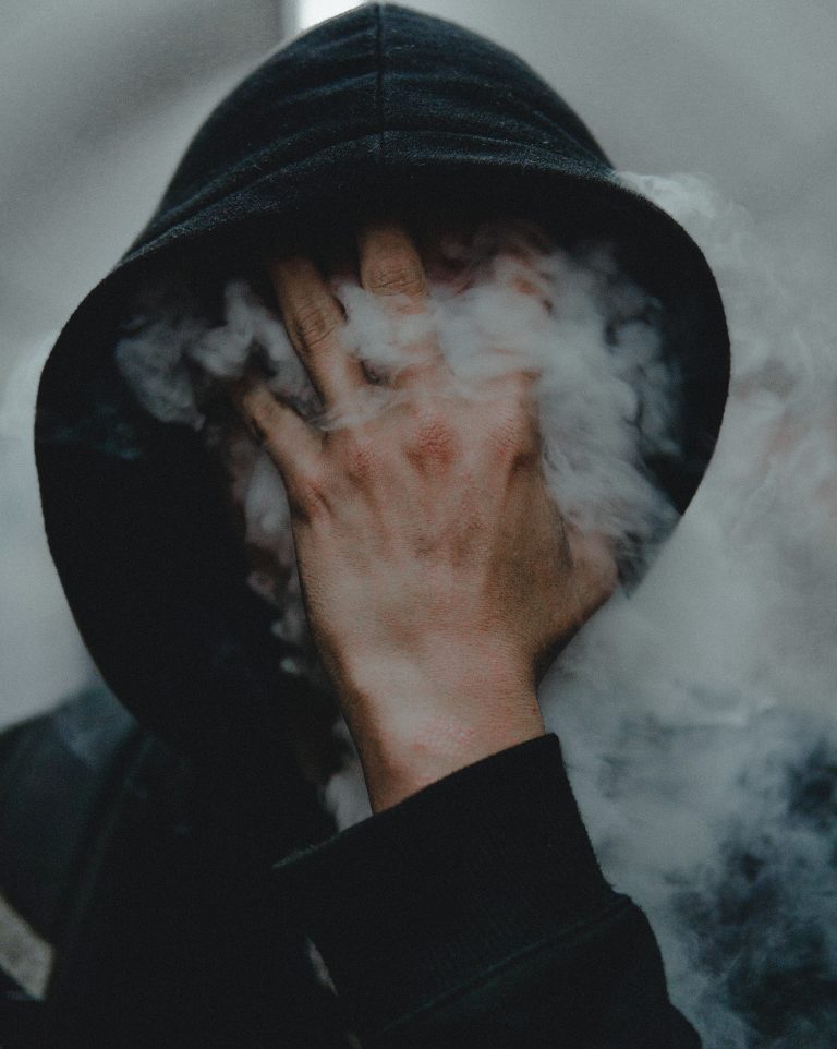 Debunking the cannabis myths - a person in a black hoodie holds their hand to their face, with smoke obscuring it.