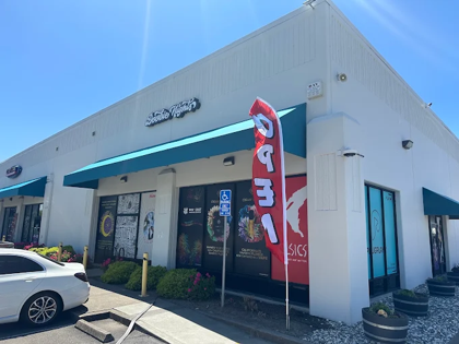 Exterior of Doobie Nights storefront with teal awnings, parked car, and a red vertical banner under a sunny blue sky