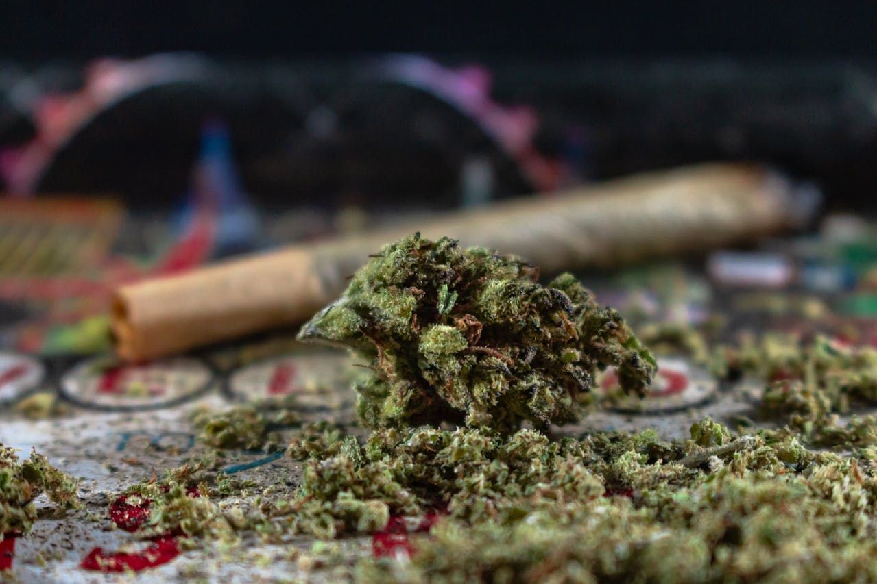 A cannabis nug in front of a rolled blunt on a table.