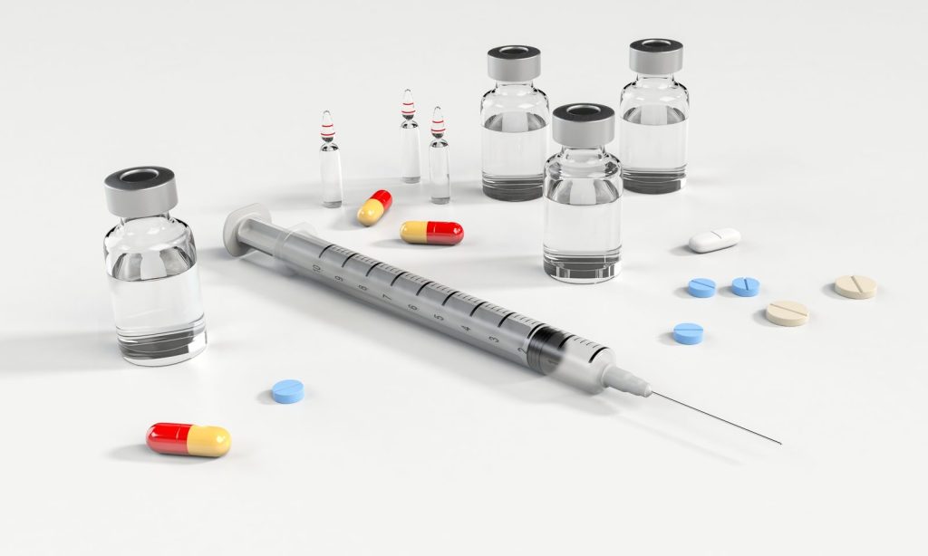 Prescription pills, glass vials and a syringe on a white surface, representing the pharmaceutical industry