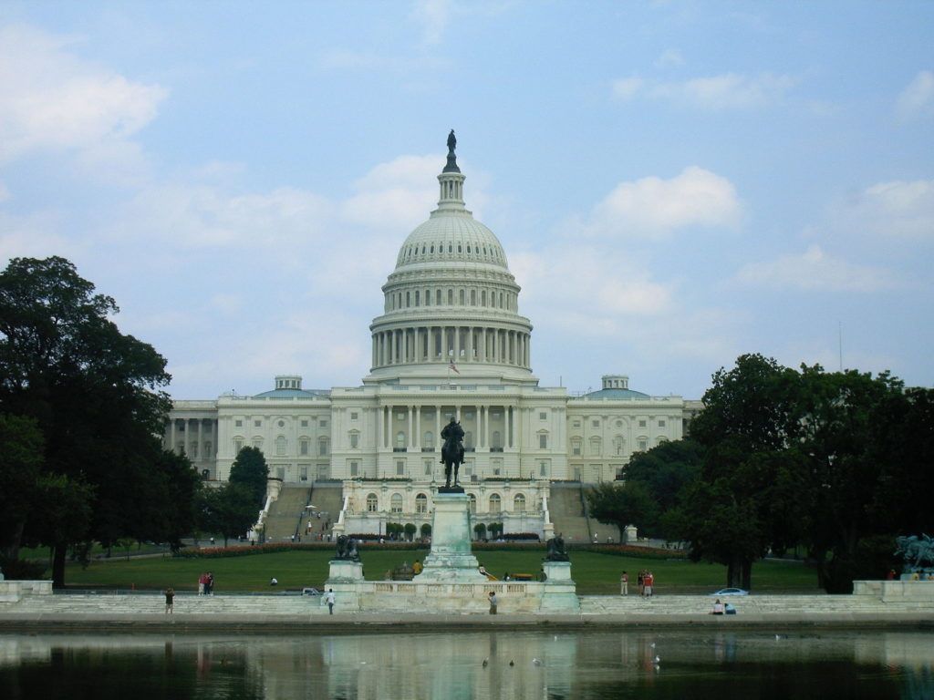 United States Capitol building in Washington, D.C., reflecting in the foreground water. The sky is partly cloudy.