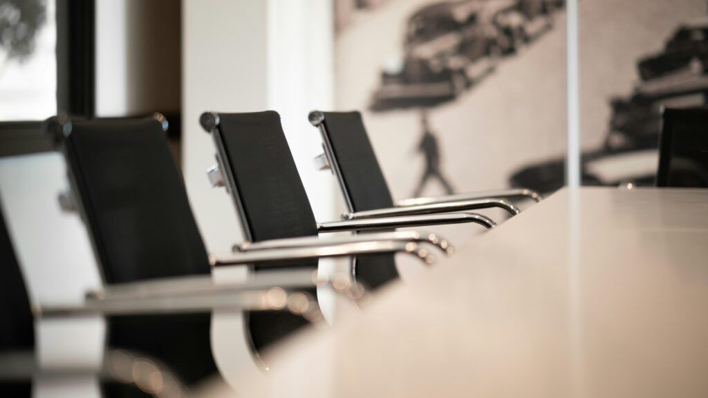 Three black leather office chairs with chrome arms and legs sit in front of a light-colored wall.